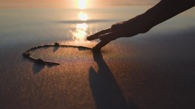 Valentine's Day. A woman's hand draws a heart on the sand. love and relationships. romantic walk on the beach at sunset.