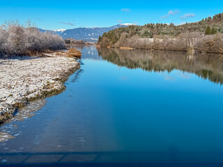 River Drava winding through Rosental valley surrounded by snow-capped mountains of Gerlitzen seen from Sankt Jakob im Rosental, Carinthia, Austria. Frozen forest and winter landscape in Austrian Alps