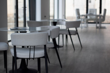 Horizontal photo. Empty light interior of cafe, cozy office room, canteen, coworking with white chair, round glass table without people. Concept of lunch, dinner, work, job, business. Desk. City day