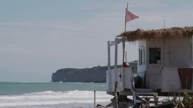 Beautiful Scenic Beach Hut Located on a Rocky Shoreline Surrounded by Flags and Calm Waters