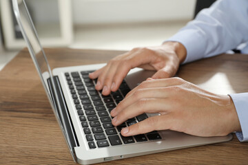 Businessman using laptop at wooden table, closeup. Modern technology