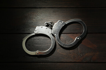 Metal chain handcuffs on wooden table, top view