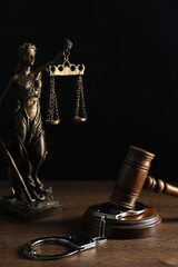Handcuffs, judge's gavel and Lady Justice figure on wooden table
