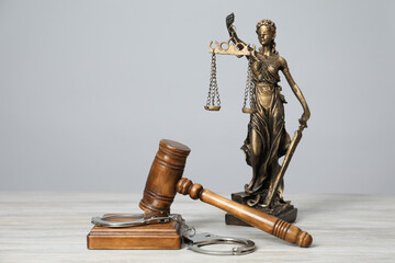 Handcuffs, judge's gavel and Lady Justice figure on white wooden table