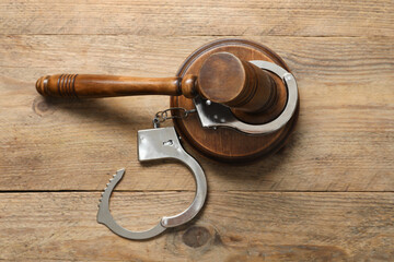 Handcuffs and judge's gavel on wooden table, flat lay