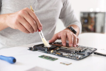 Man cleaning motherboard with brush at white table, closeup