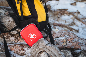 Next to a backpack, there is a prominently displayed red first aid kit featuring a white cross...