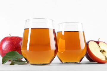Fresh apple juice in glasses, fruits and green leaves on white table, closeup