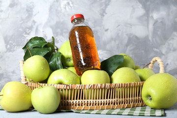 Tasty apple juice in glass bottle, green leaves and fresh fruits on grey table