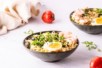 Ramen noodles with egg, shrimps, greens, seasame, seaweed and spices on white marble table close up. Traditional Asian soup.
