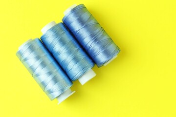 Spools of colorful sewing threads on yellow background, flat lay. Space for text