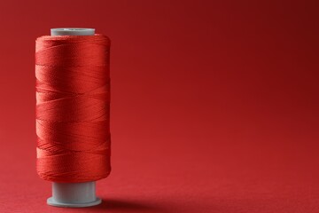 Spool of colorful sewing thread on red background, space for text