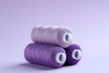 Spools of colorful sewing threads on lilac background, closeup