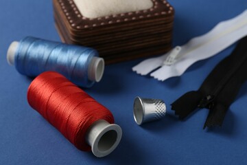 Different sewing supplies on blue background, closeup