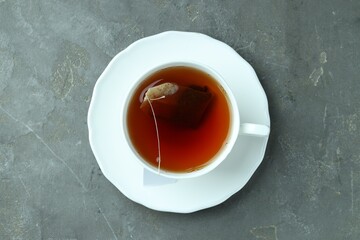 Tea bag in cup with hot drink on gray textured table, top view