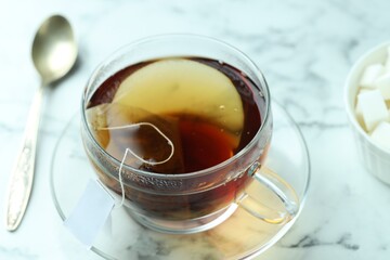Tea bag in glass cup with hot drink and spoon on light marble table, closeup