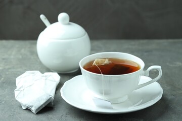 Tea bag and cup with hot drink on gray textured table