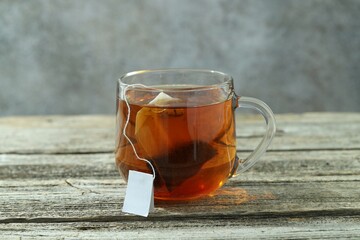 Tea bag in glass cup with hot drink on wooden table against gray background