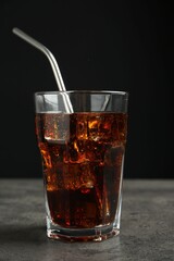 Cold cola with ice cubes and drinking straw in glass on grey table against black background, closeup