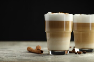 Tasty latte macchiato in glasses, coffee beans and cinnamon on grey table, closeup. Space for text