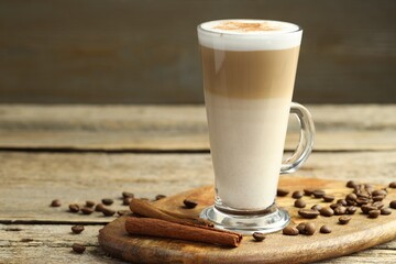 Tasty latte macchiato in glass cup, coffee beans and cinnamon on wooden table, closeup. Space for text