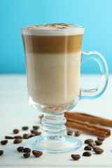 Tasty latte macchiato in glass cup, coffee beans and cinnamon on white wooden table, closeup