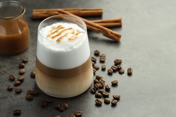 Tasty latte macchiato in glass, coffee beans and cinnamon on grey table, closeup. Space for text