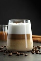 Tasty latte macchiato in glass, coffee beans and cinnamon on grey table, closeup