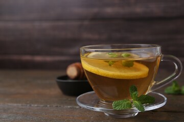 Tasty mint tea in cup, lemon and fresh leaves on wooden table, closeup. Space for text