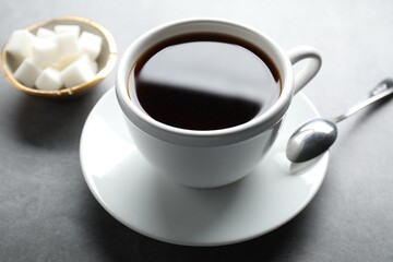 Refreshing black tea in cup, spoon and sugar cubes on grey table, closeup
