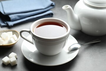Refreshing black tea in cup and sugar cubes on grey textured table, closeup