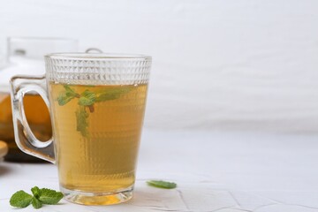 Aromatic mint tea and fresh leaves on white textured table, closeup. Space for text