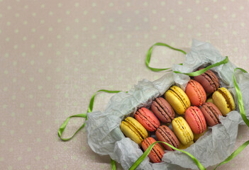 colorful macaroons cakes packed in a box with ribbon on a yellow polka dot background, space for text