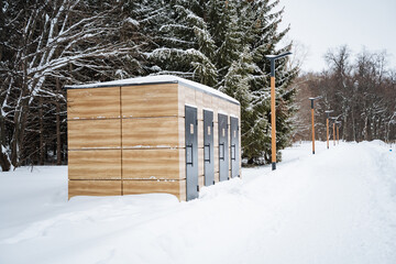 A rustic wooden shed is sitting quietly in the middle of a snowy forest, surrounded by tall trees,...