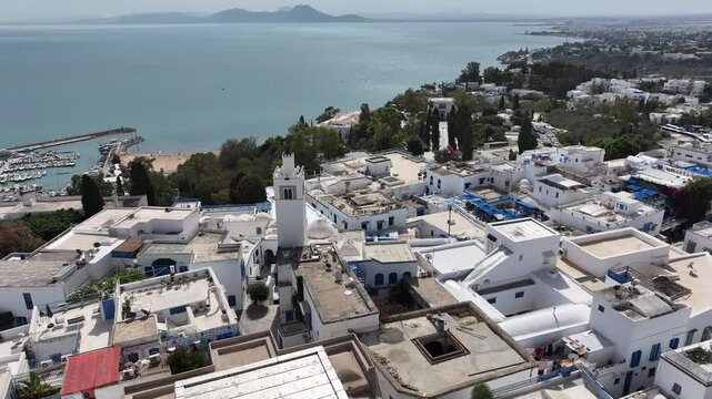 Picturesque aerial footage of Sidi Bou Said, Tunisia, featuring its whitewashed walls, iconic blue doors, cobbled streets, and breathtaking views of the Mediterranean coastline under a clear sky.