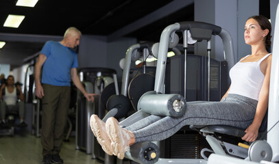 Girl in sportswear trains his leg muscles on a machine in the gym