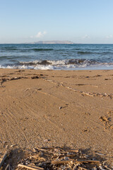 Sandy beach with waves. Close-up view of sand with sea waves and an island in the background