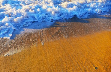 Sea waves with foam and sandy beach in golden sunset in coastline