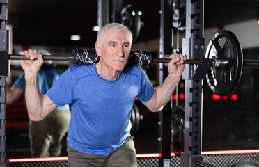 Elderly athletic man lifting heavy barbell in gym