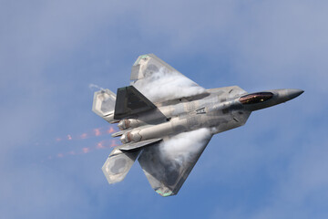 Close top view of a F-22 Raptor in beautiful light in a turn, with condensation clouds at the wing...
