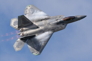 Close top view of a F-22 Raptor in beautiful light in a turn, with condensation clouds at the wing...