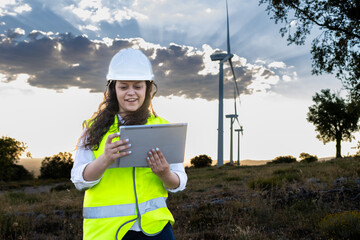 Female engineer using tablet at wind farm during sunset