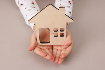 Adoption. Little girl with house figure at beige table, closeup