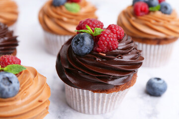 Tasty cupcakes with chocolate cream and berries on white marble table, closeup