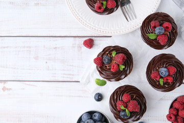 Tasty cupcakes with chocolate cream and berries on white wooden table, flat lay. Space for text