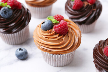 Tasty cupcakes with chocolate cream and berries on white marble table, closeup