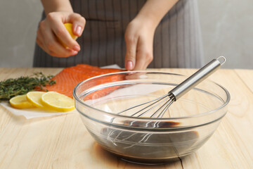 Woman squeezing lemon juice onto salmon fillet wooden at table, focus on bowl with soy sauce