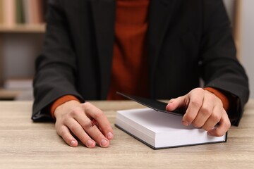 Signing autograph. Writer with pen and book at wooden table indoors, closeup