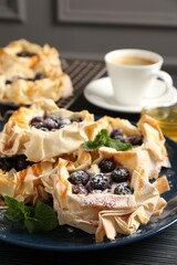 Tasty puff pastries with blueberries, powdered sugar, mint, coffee and honey on dark table, closeup