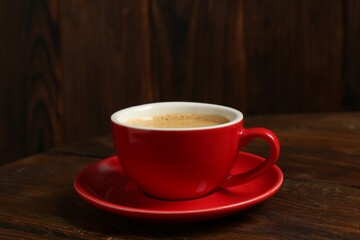 Red cup with coffee on wooden table, closeup